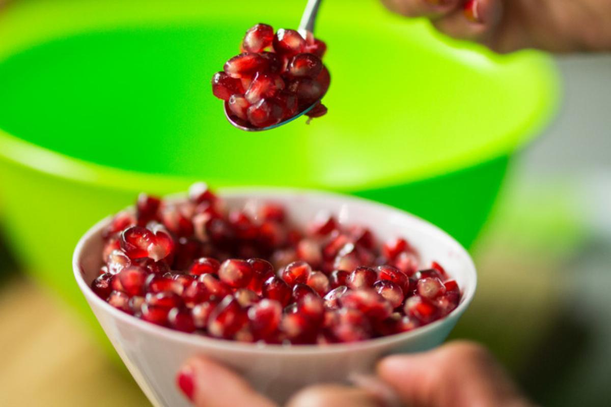 Pomegranate is a superfood that provides heart-healthy antioxidants A woman takes a teaspoon of pomegranate seeds from a bowl she holds in her left hand