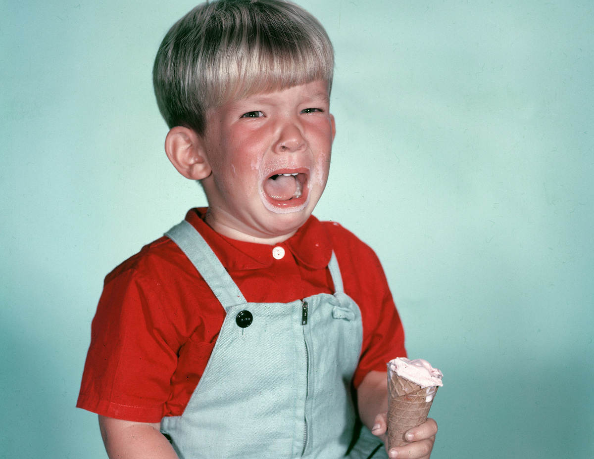 ice cream mouth burn-2953777 Studio portrait of a young boy crying as he holds a melting ice cream cone, circa 1962.