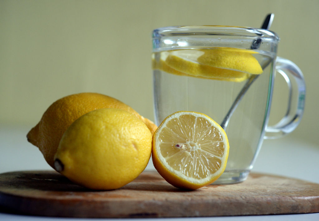 A glass of lemon water is pictured near sliced lemons