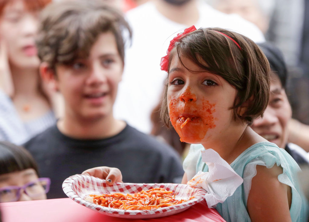 A young girl eating pasta wears sauce all over her mouth
