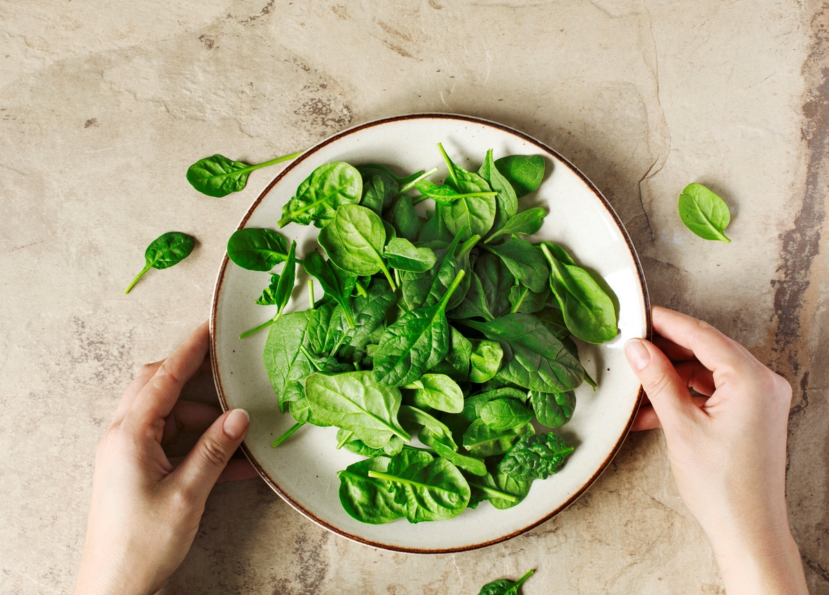 bowl of spinach - 1147808702 Woman sets a plate full of spinach down on a table.