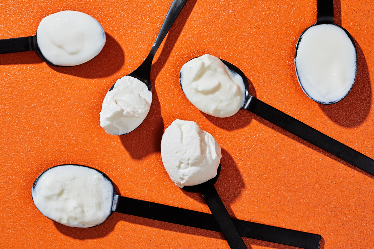 spoonfuls of yogurt - 1167954483 Spoonfuls of yogurt lie against an orange table.