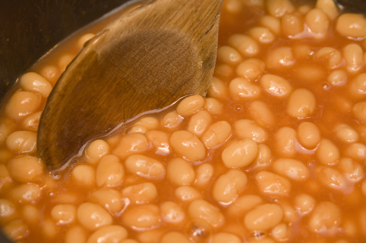baked beans - 157876671 A wooden spoon mixes a pot of baked beans.