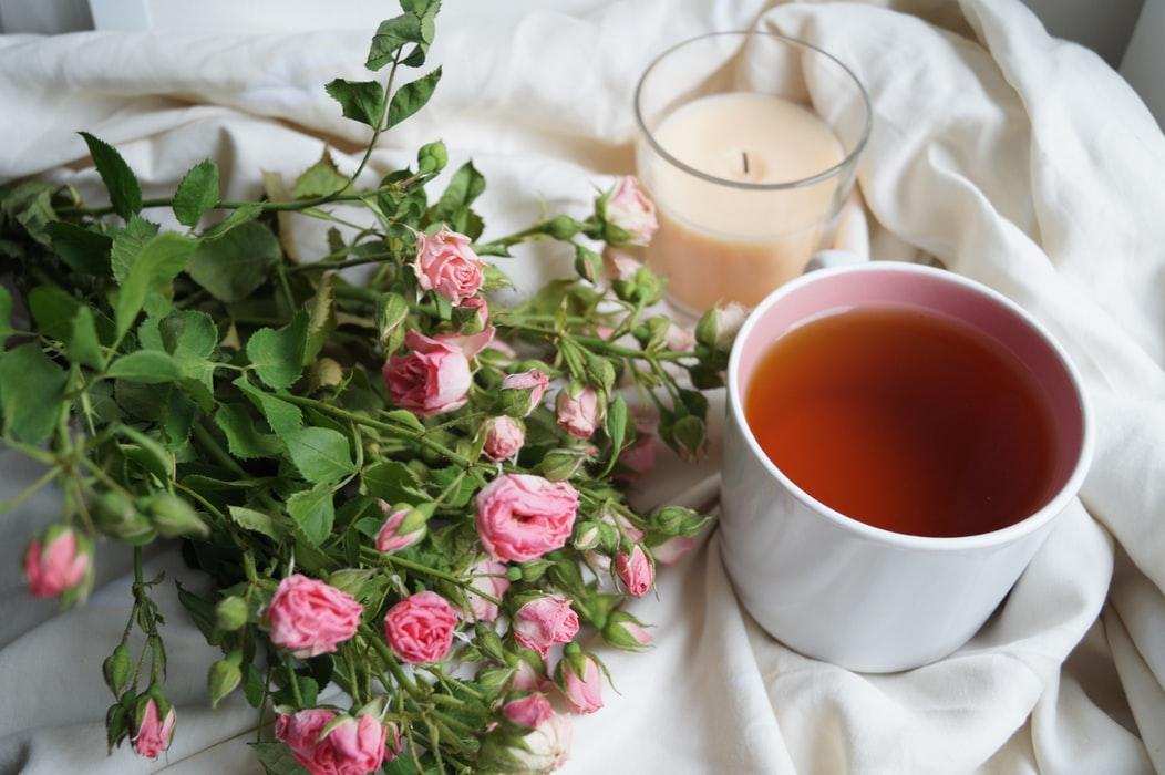 passionfruit tea A cup of passionfruit tea sits on a bed next to a candle and flowers.