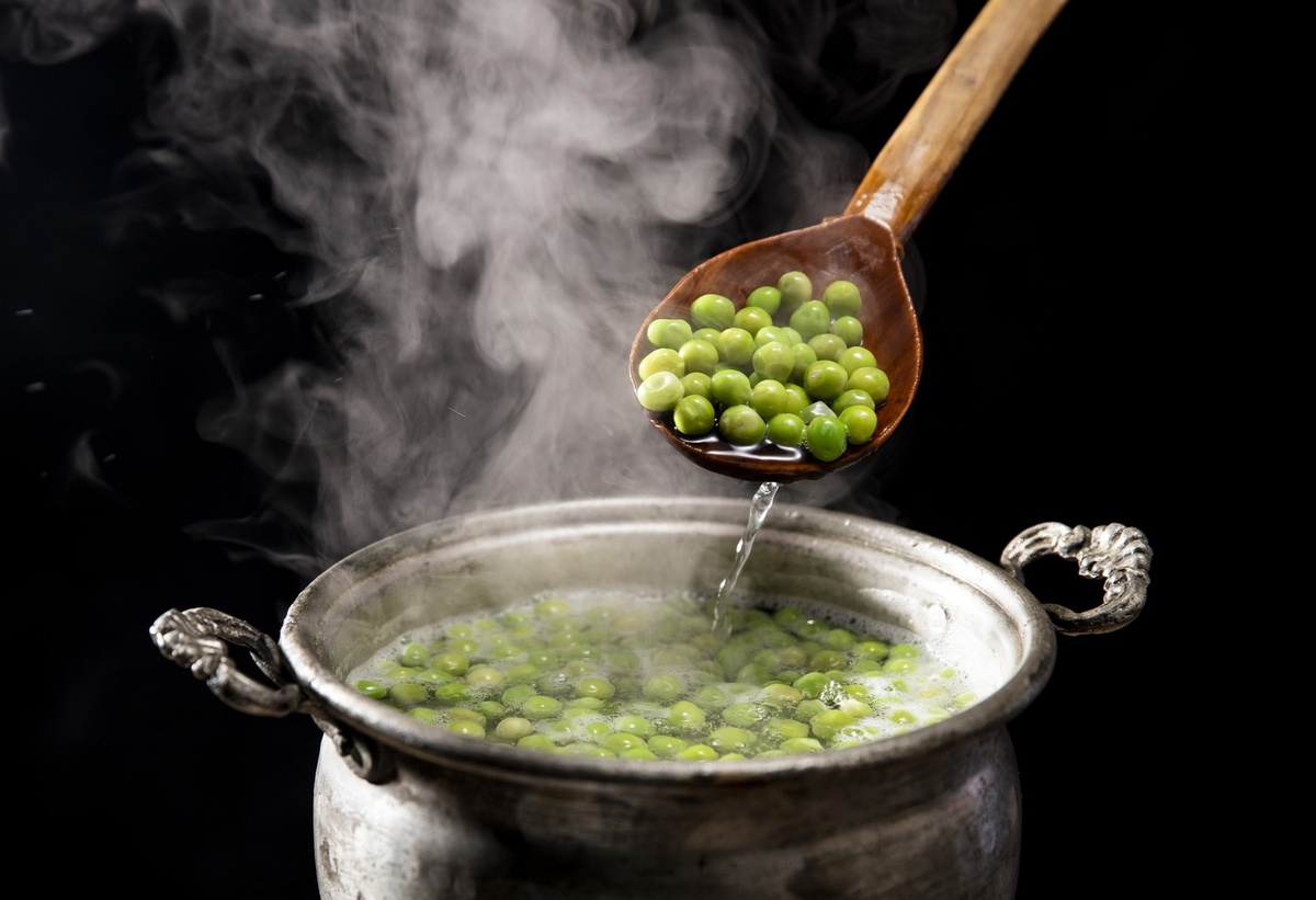 peas Cooked peas are dished out of a pot with a wooden spoon.