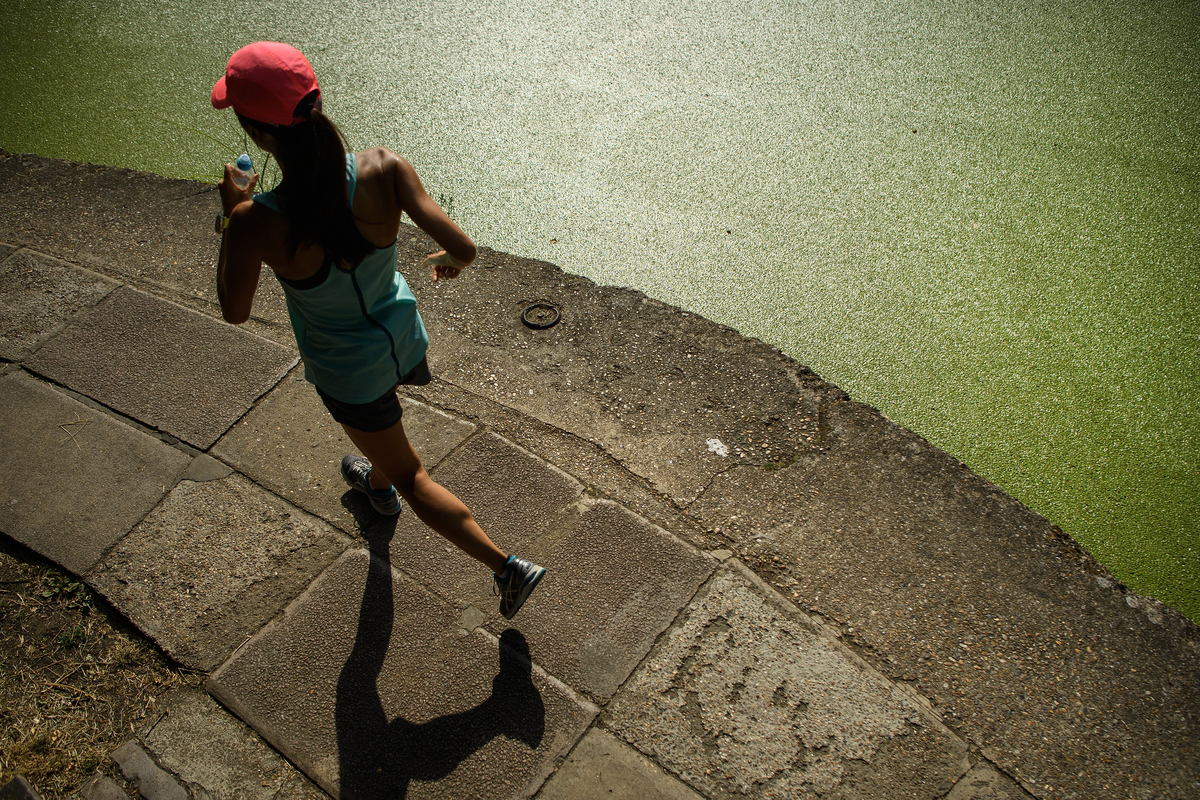 jogging - 1004515588 A jogger runs past the green coating on Regent's Canal following a huge increase in the amount of duck weed