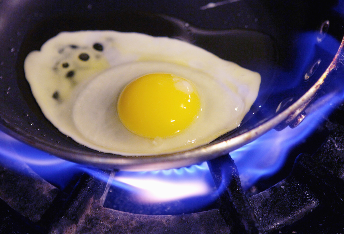 frying an egg - 103646958 An egg fries in a pan.