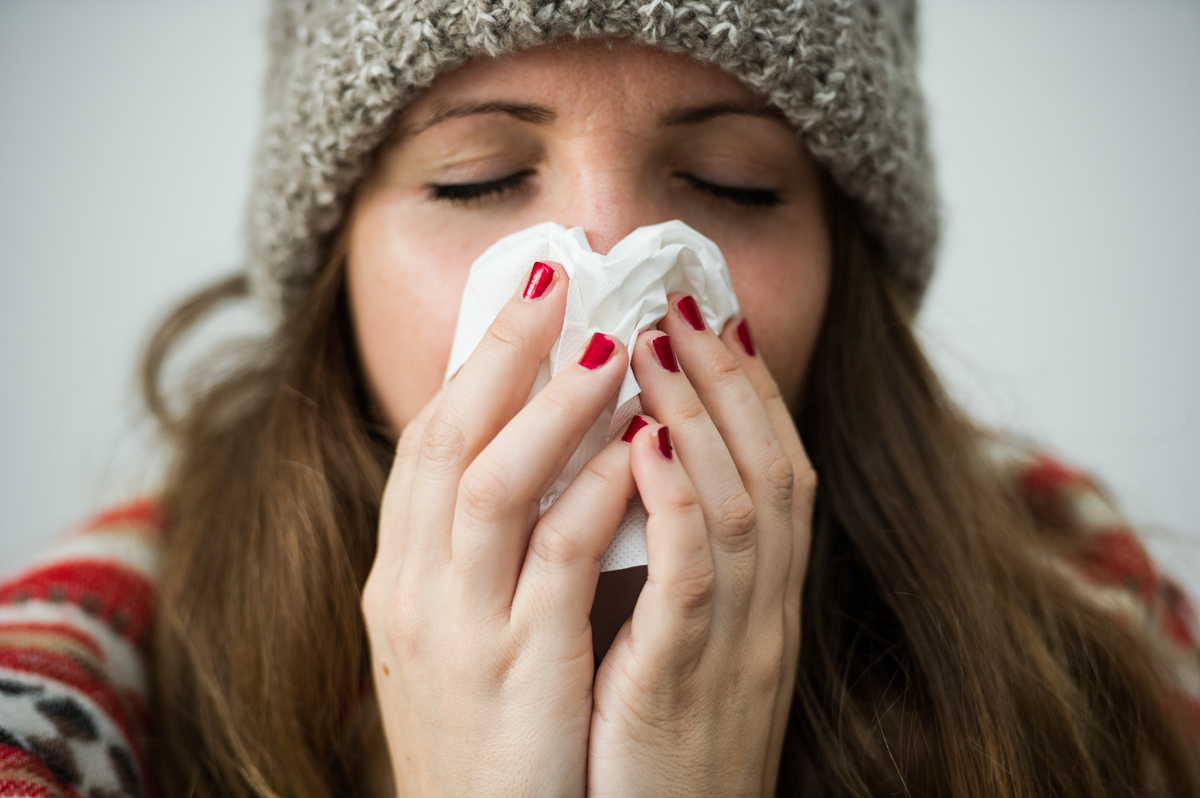blowing nose - 1038950058 A young woman uses a tissue to blow her nose.