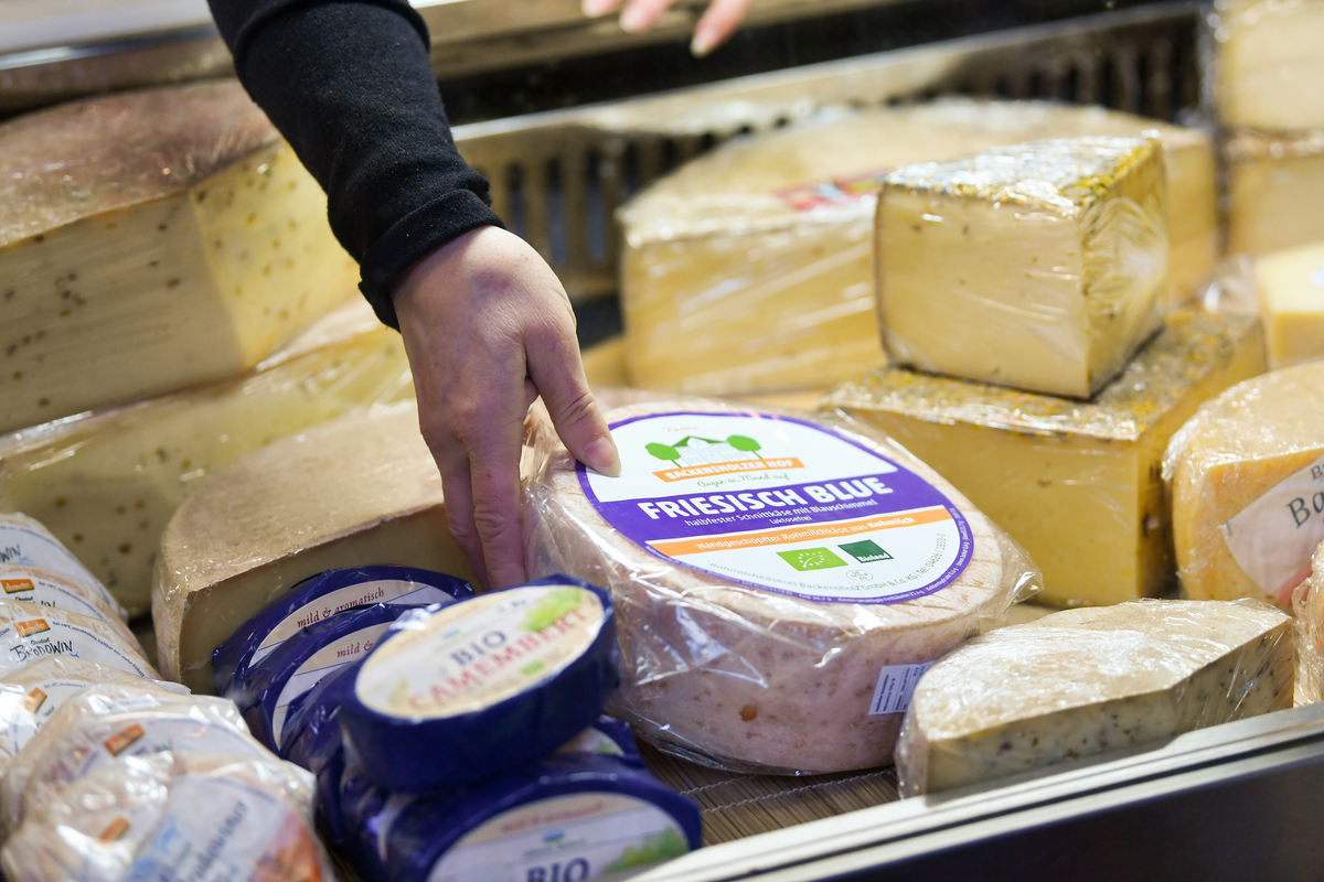 reaching for cheese - 1086747890 A saleswoman reaches for a cheese wheel.