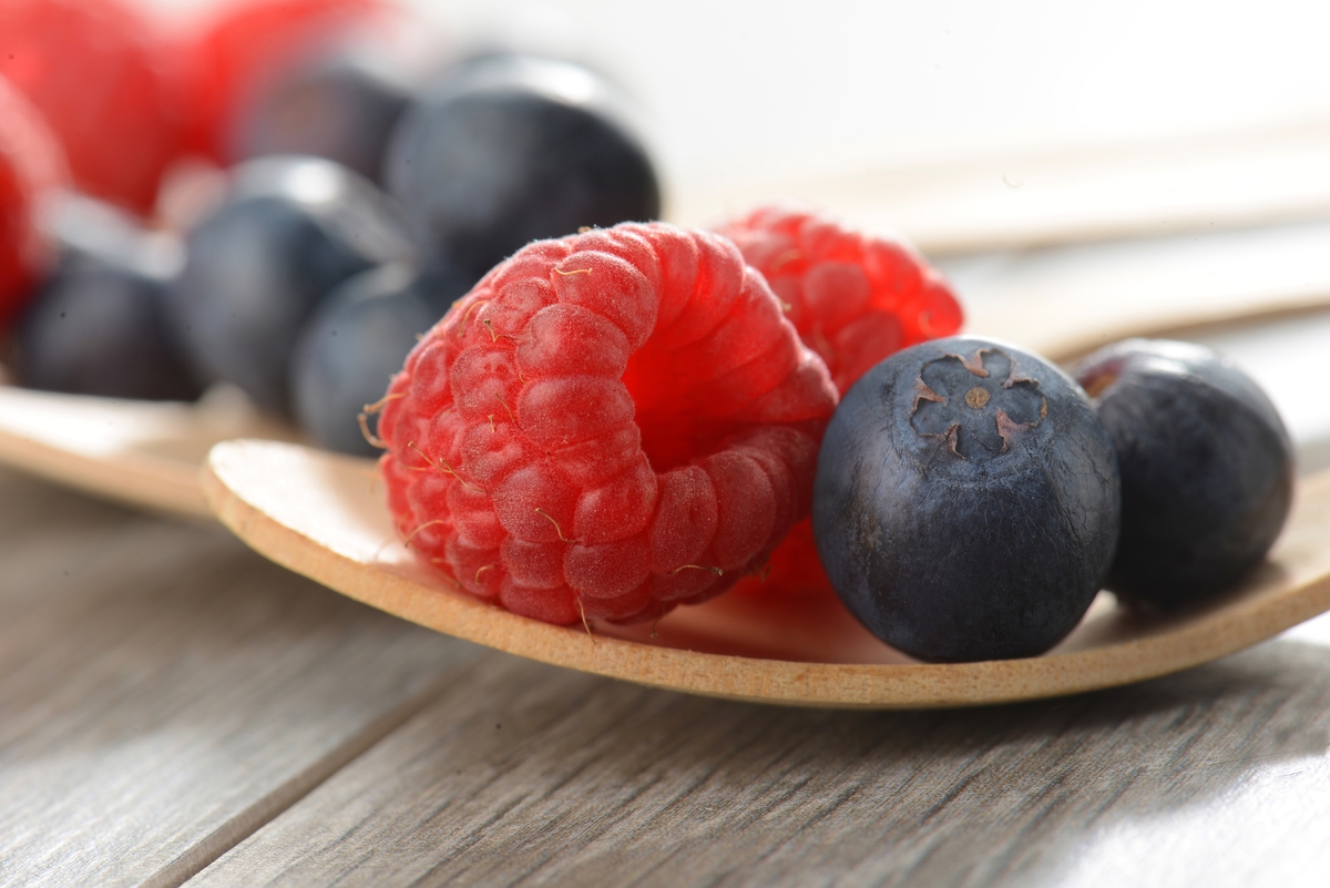 rapberries and blueberries - 1147955159 A small wooden plate holds raspberries and blueberries.