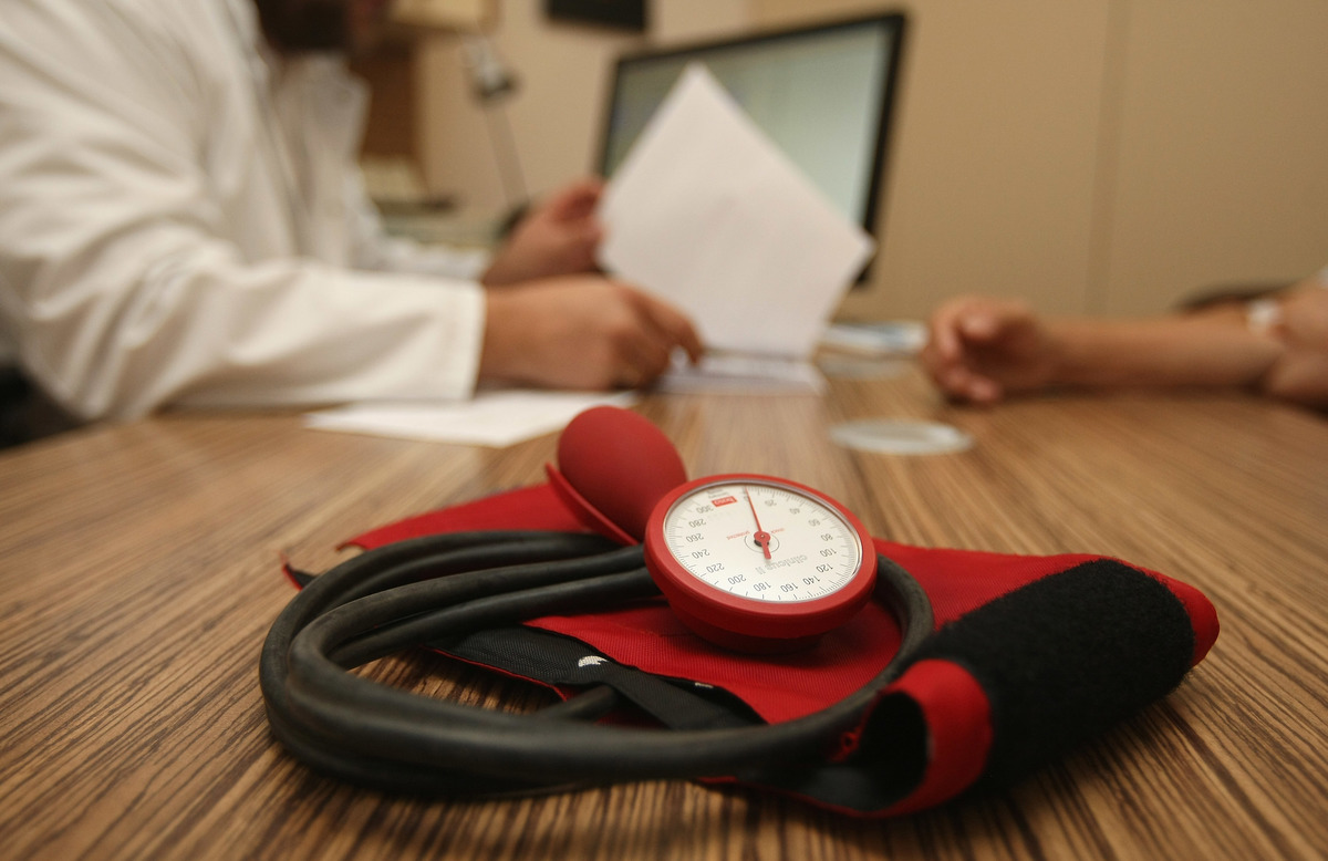 sphygmomanometer - 151262809 A doctor speaks to a patient as a sphygmomanometer, or blood pressure meter, lies on his desk.