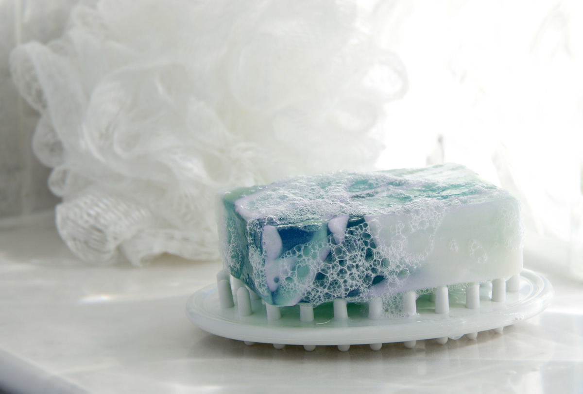 glycerin soap - 170501502 A bar of glycerin soap rests on a soap dish in front of a loofah.