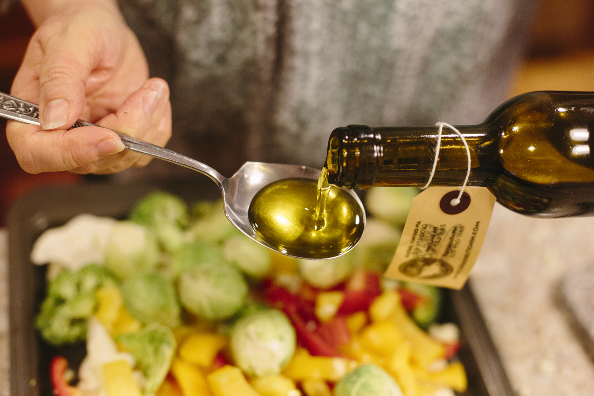 olive oil in a spoon - 465218438 Woman pours out olive oil infused with a butter flavoring over a pan of cauliflower, brussels sprouts, red and yellow peppers and broccoli.