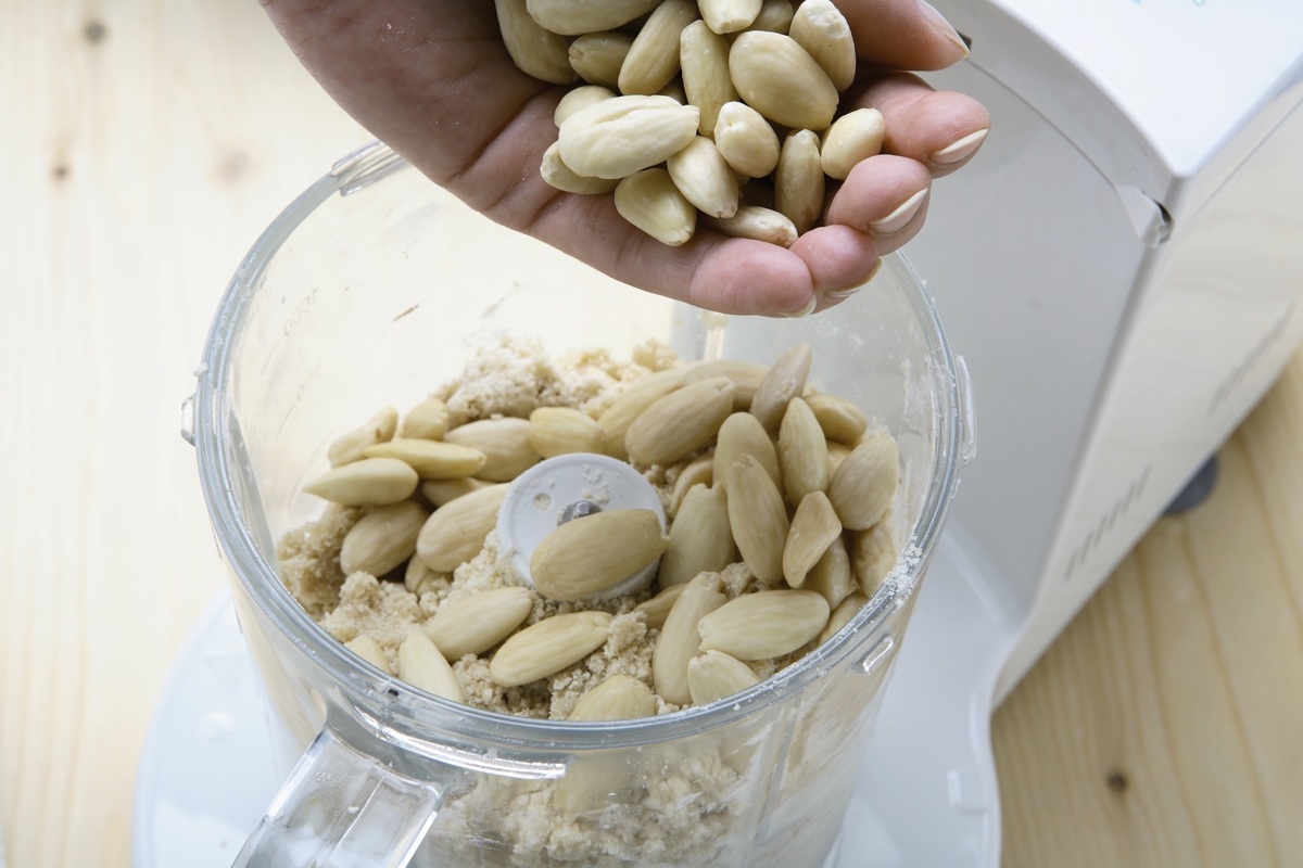 peeled and crumbled almonds - 494801545 A woman placed peeled almonds in a blender to create a crumble.