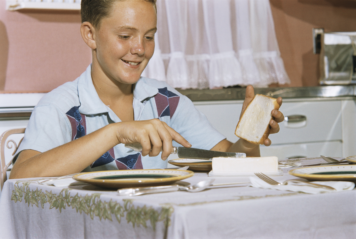 buttering bread - 524757044 A boy spreads butter on white bread.