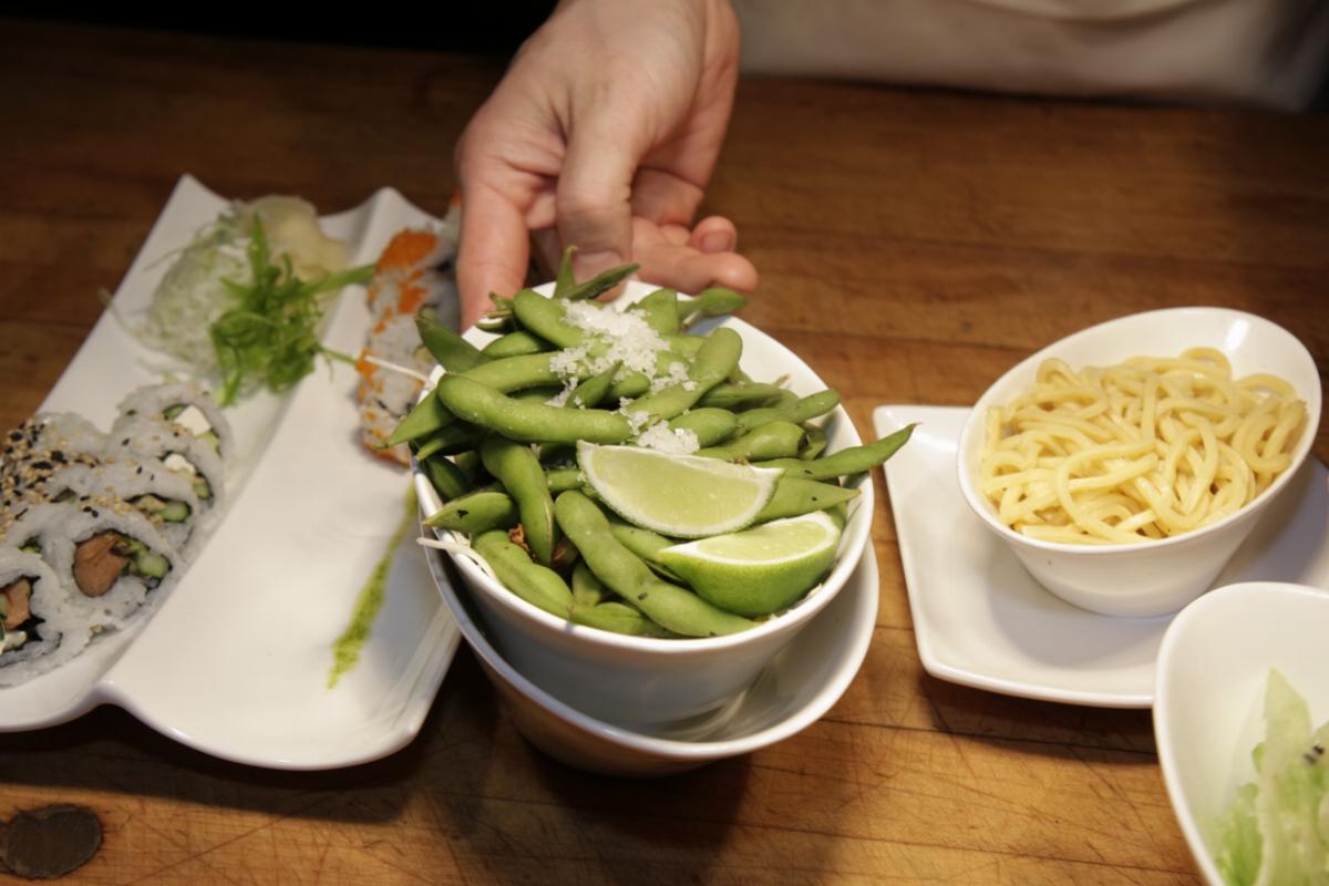 bowl of soy - 838273558 A person holds a bowl of soy over a meal of sushi and low mein.