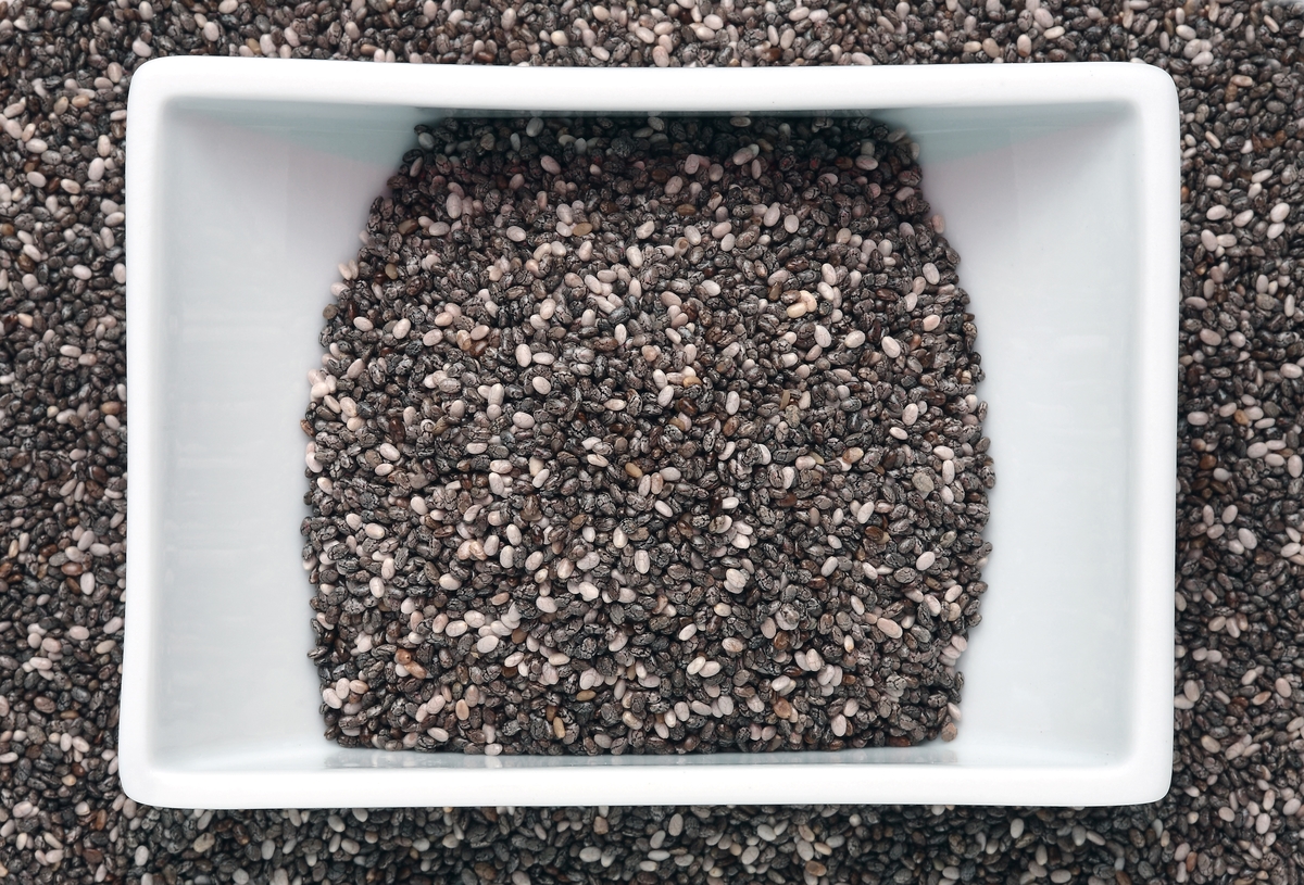 bowl of chia seeds - 849795212 A sqaure-shaped bowl of chia seeds rests on more chia seeds.