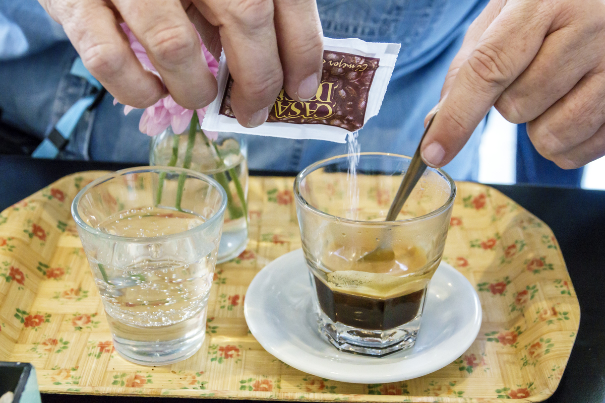 sugar in espresso - 982747136 Person pours sugar into an espresso coffee.