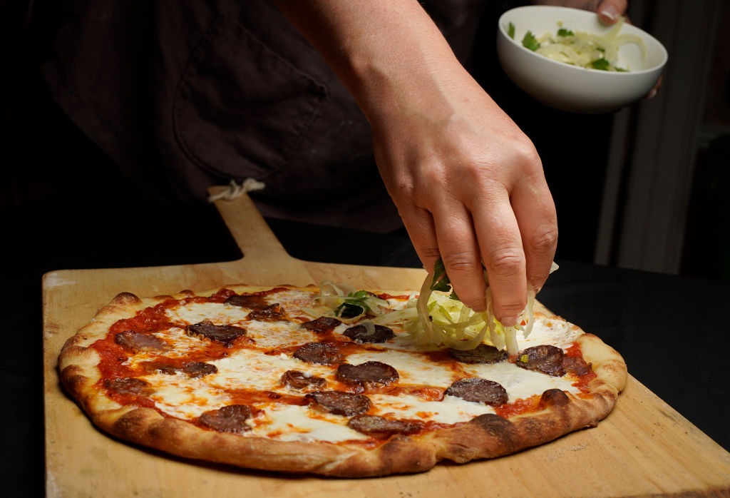 pizza 1180678275 someone putting toppings on a pizza