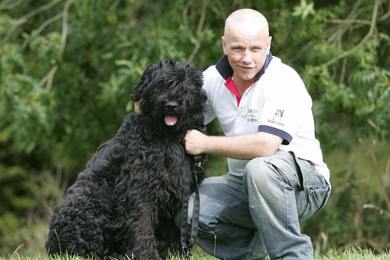 black-russian-terrier A Black Russian Terrier sits in the grass next to its owner.