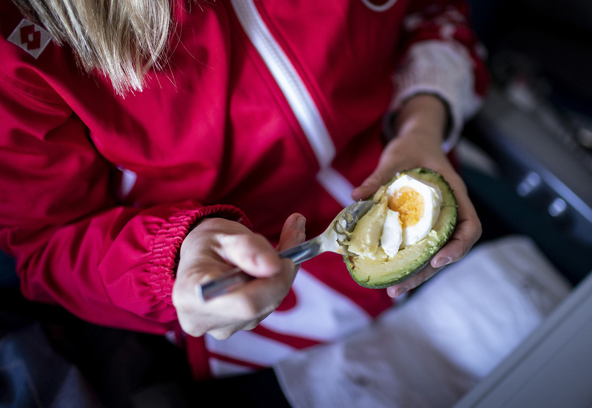 avocado and egg - 1093539854 A woman eats a hard-boiled egg in an avocado.