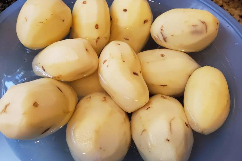 soaking potaotes - 1192967632 Peeled potatoes soak in water in a blue bowl.