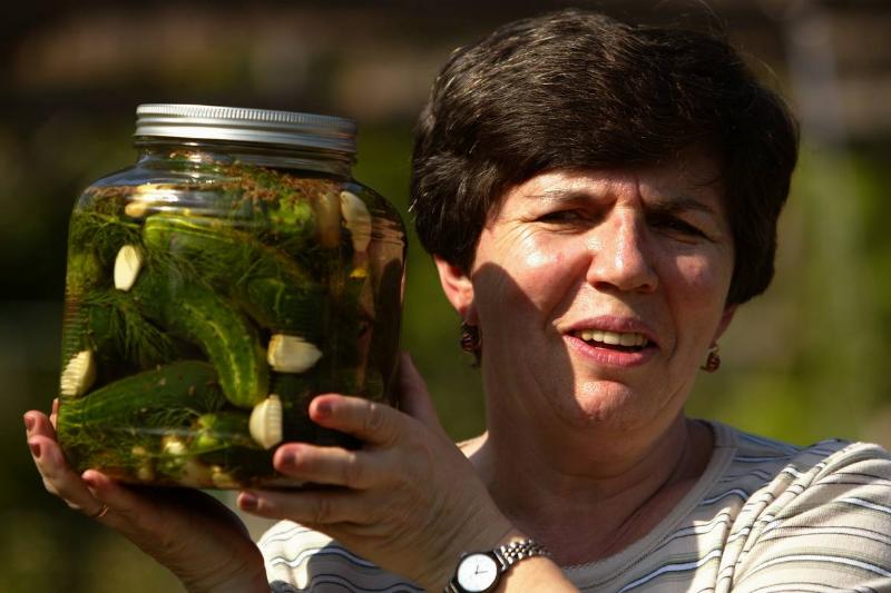pickle juice - 563606829 A woman holds up a jar of dill pickles.