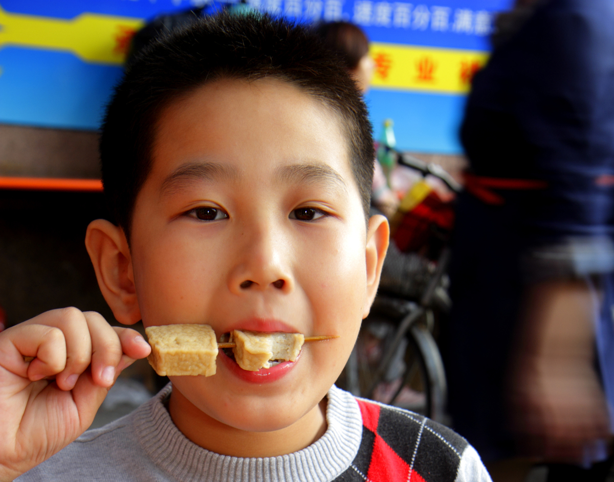 eating tofu - 586124552 A young boy eats tofu on a stick.