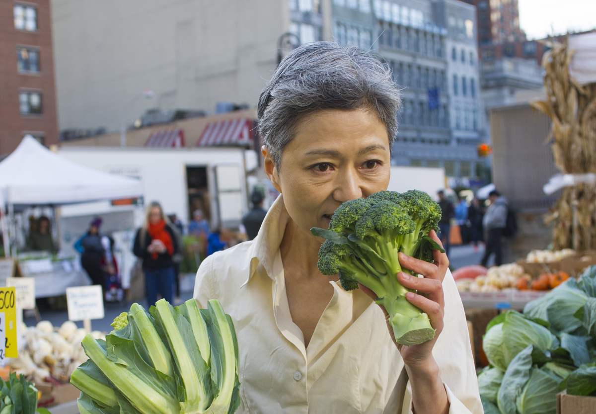 smelling broccoli - 661870626 A woman smells fresh broccoli at a farmer's market.