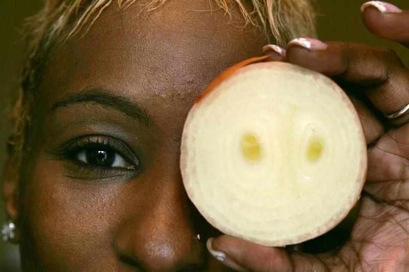 onion slice - 831784632 A woman holds up a white onion in front of her eye.