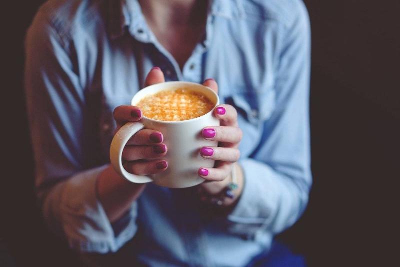 holding coffee A woman in a blue shirt holds a latte in a mug.