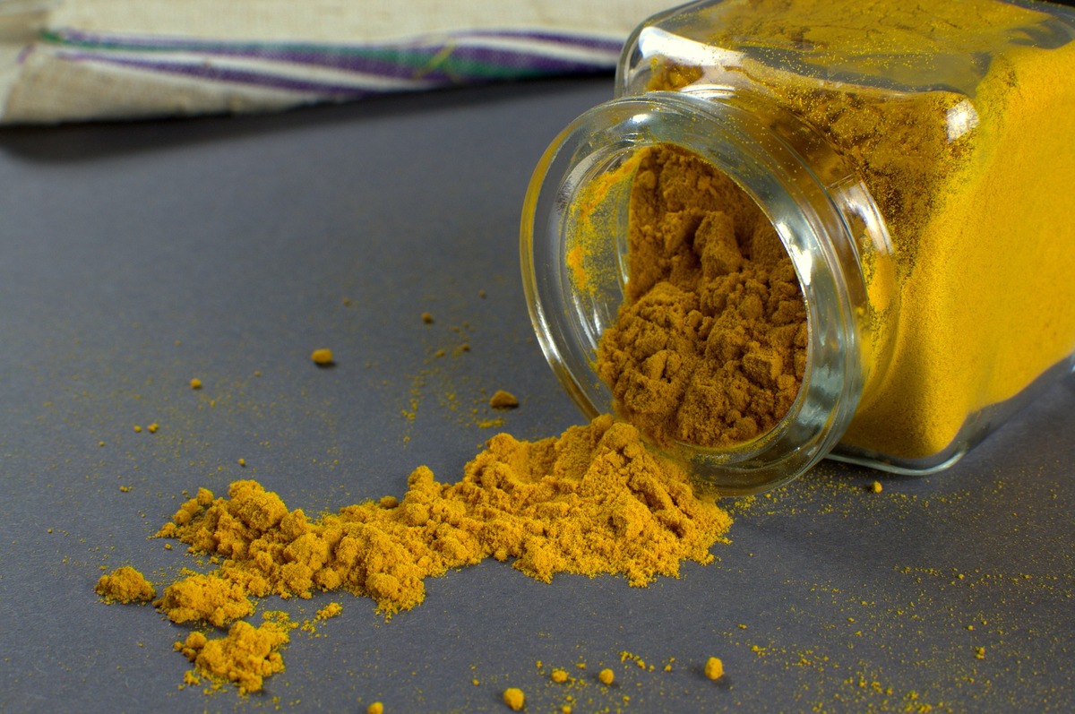 turmeric A glass container of turmeric spills onto a table.