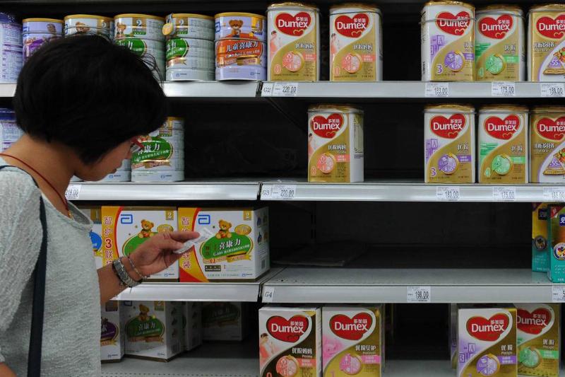 baby formula -175611638 A woman checks the price beside a shelf of Dumex baby formula