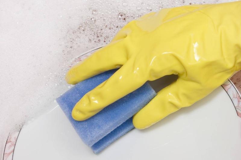 washing dishes-544598359 A person wearing gloves washes a dish with a sponge.