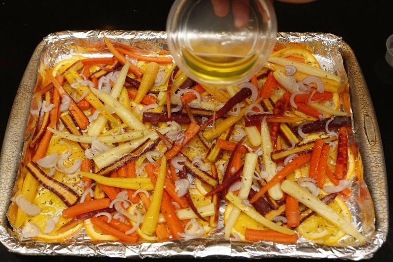 roasted carrots - 567363279 A person pours olive oil onto a pan of carrots to roast.