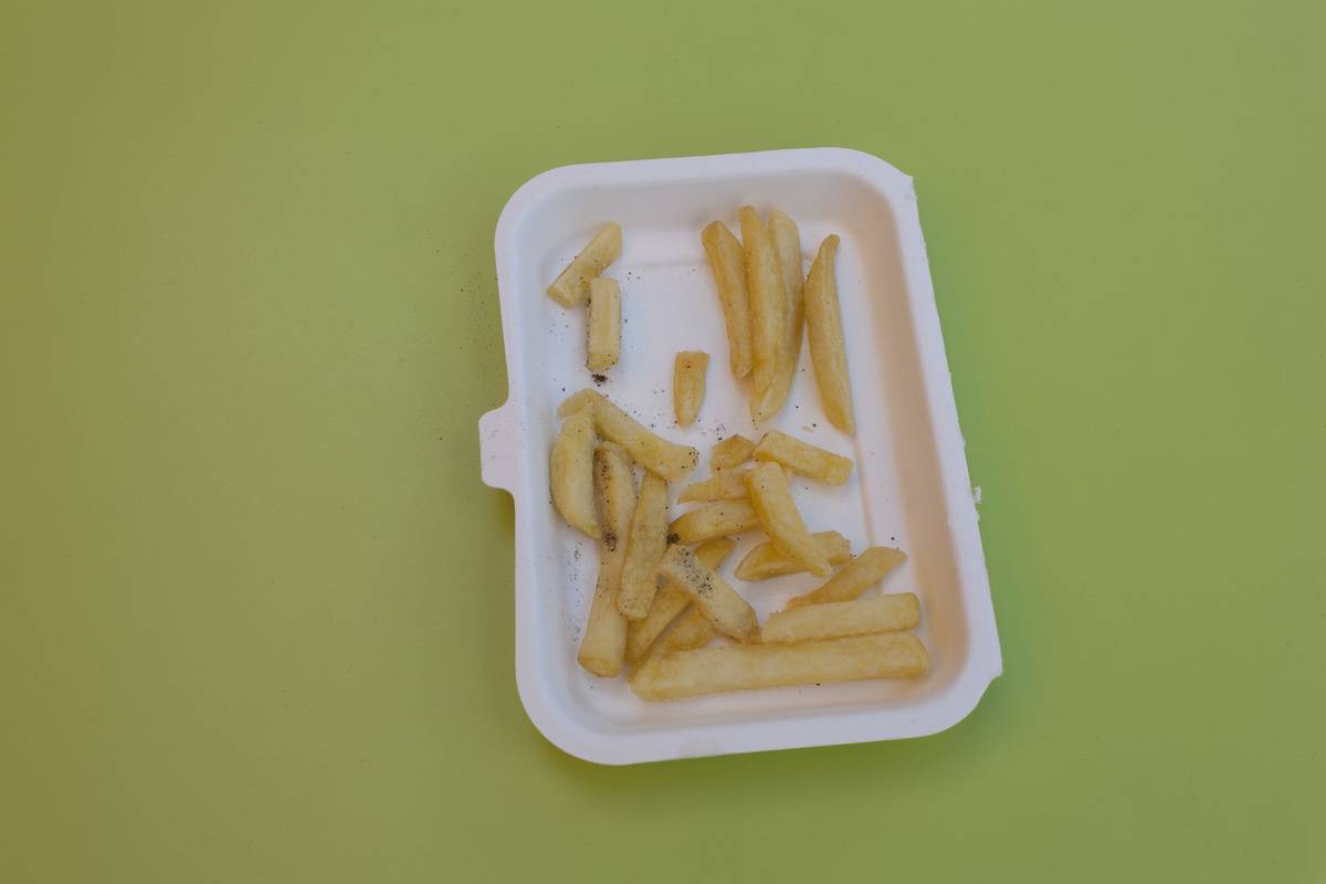A detail of half-eaten fries is left in a styrofoam dish on a green cafe table.