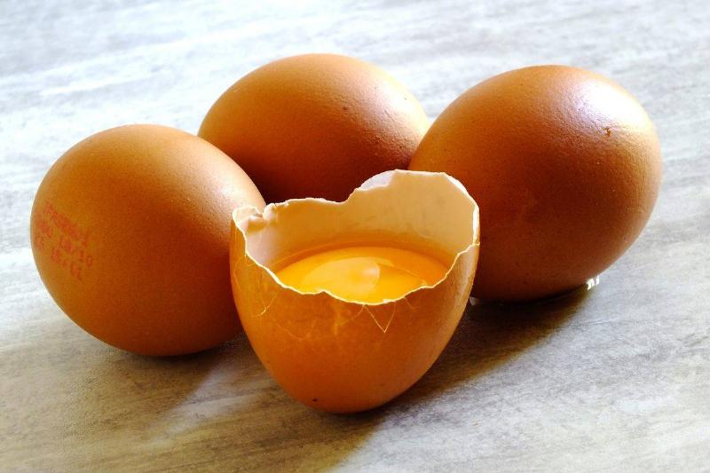 Four brown eggs site on a table; one is broken open.
