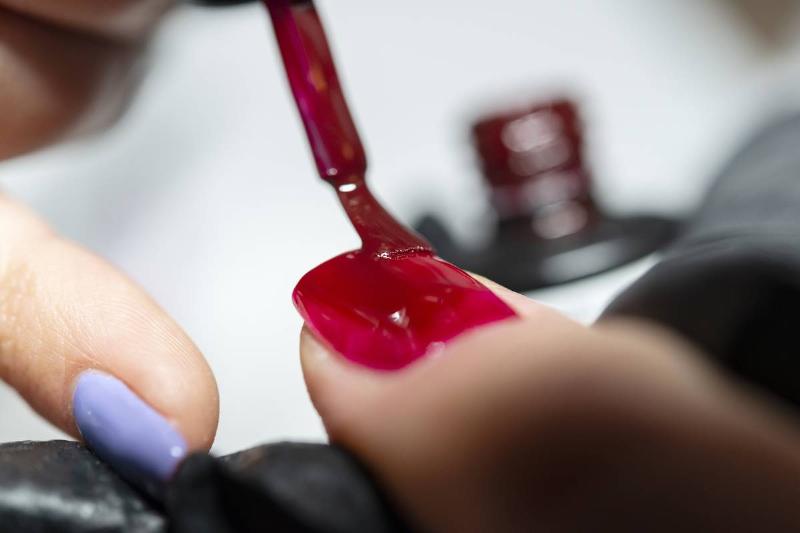 painted nails - 1147761438 A nail technician applies red polish onto a woman's thumb nail.