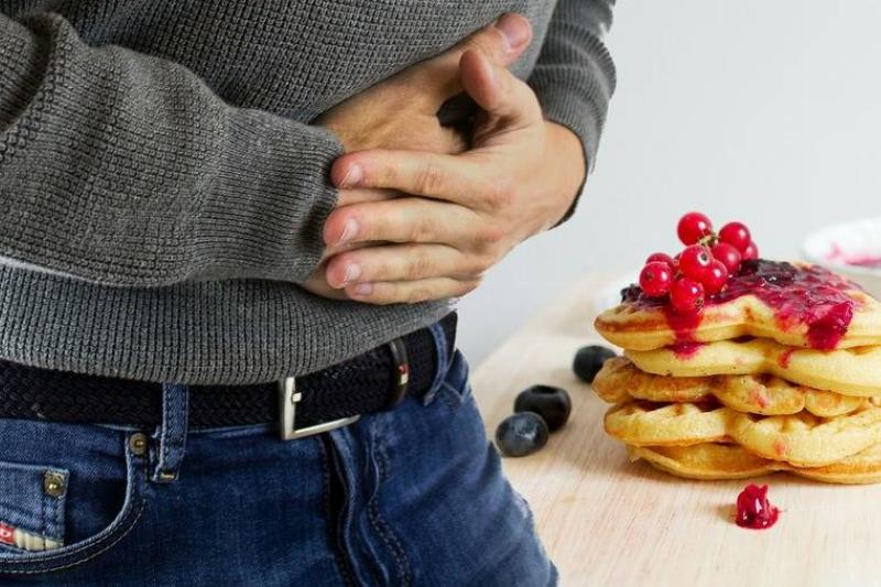 hunger signs a man holding his stomach while looking at a stack of waffles