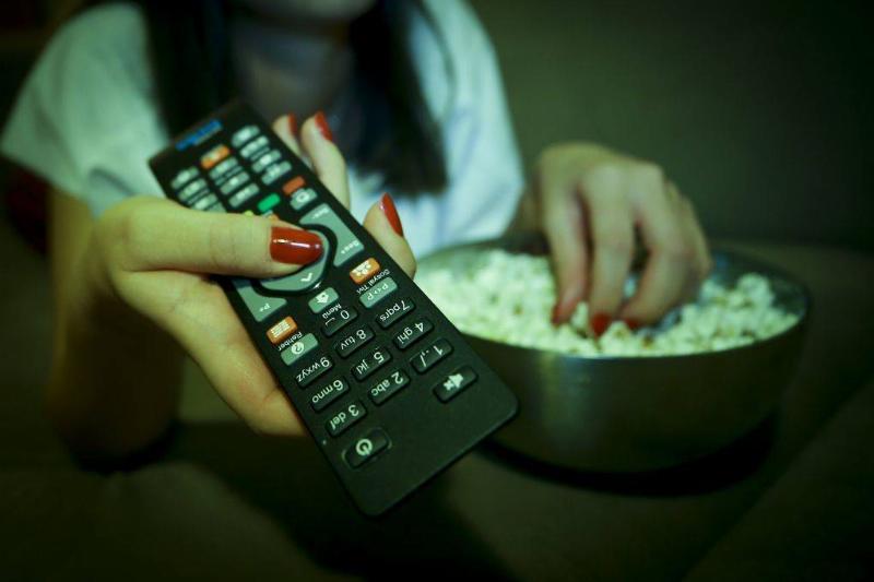 tv remote 1065620216 A woman holds a remote controller while eating popcorn
