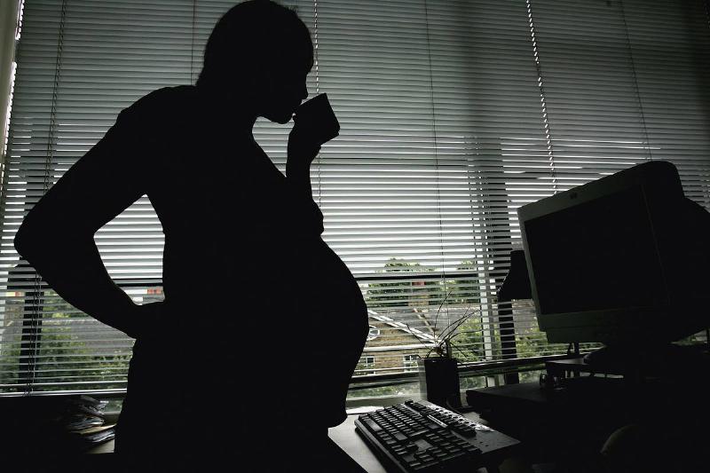 pregnant woman-53252480 A pregnant woman sips from a mug while standing at a desk.