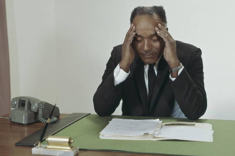stress-931845424 A businessman presses his fingers against his temple while sitting as his desk.