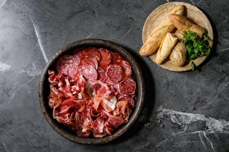 Antipasto meat platter assorti of sliced jamon, salami, chorizo sausage in terracotta tray with bread and greens over black marble background. Flat lay, space Antipasto meat platter assorti of sliced jamon, salami, chorizo sausage in terracotta tray with bread and greens over black marble background. Flat lay, space
