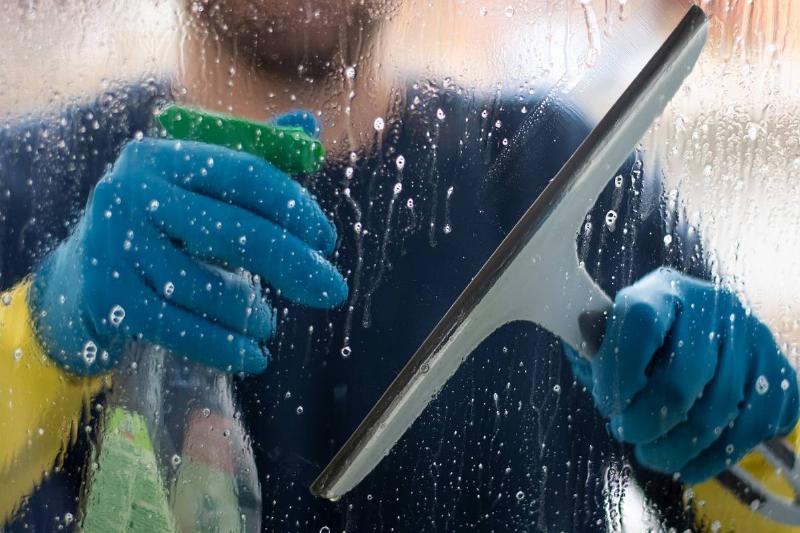 GettyImages-1128700235 window washer using squeegee outside someone washing window from outside with squeegee
