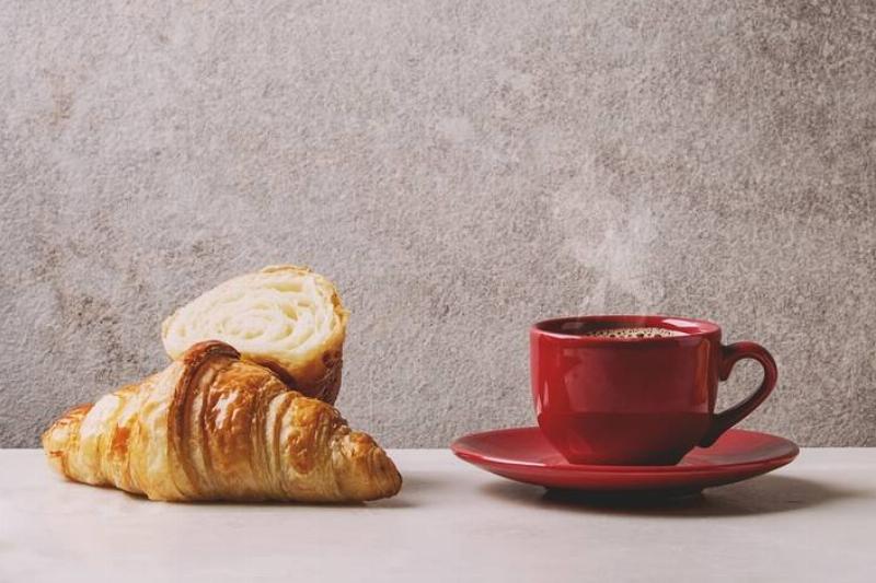 coffee mug A red mug of coffee sits next to croissants.