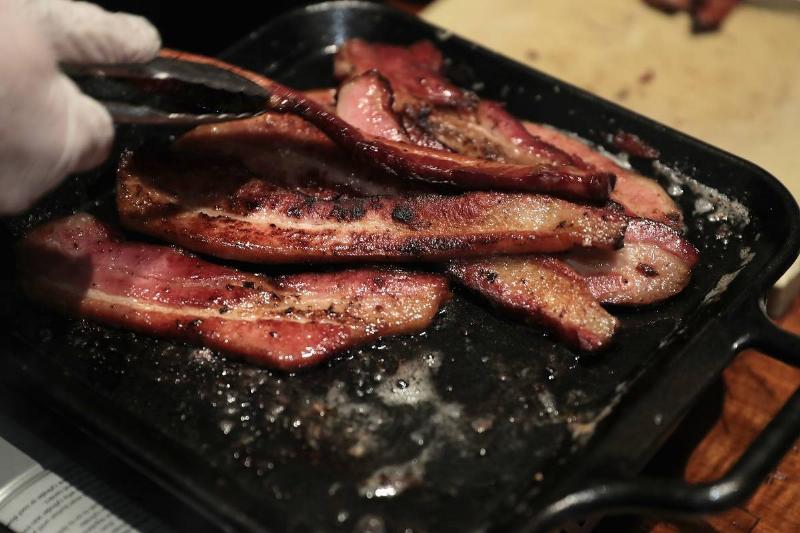 cooking bacon-620171742 A person cooks bacon on a stove.