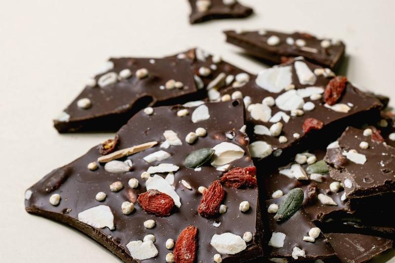 Handmade chopped dark chocolate with different superfood additives seeds and goji berries over beige background. Handmade chopped dark chocolate with different superfood additives seeds and goji berries over beige background.
