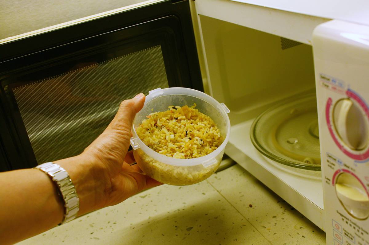 leftovers A woman puts a container of leftover rice into the microwave.