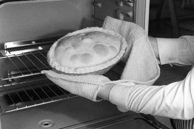 A woman takes a pie out of the oven with pot holders.