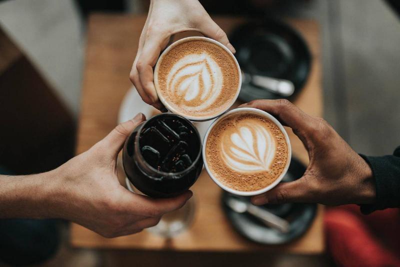 Three people press their coffee cups together to cheer.